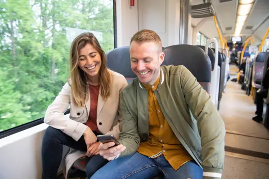 Man en vrouw zitten in trein kijkend naar telefoon